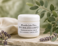 A white jar of Meadowlake Farm Hive Isolates Complex Propolis Facial Cream sits on a light stone surface, surrounded by green leaves, lavender sprigs, and a soft beige cloth in a natural, softly lit setting.